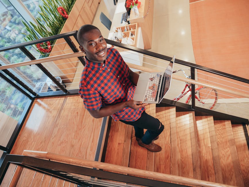 Does SoFi Actually Help Build an Emergency Fund? Smiling adult with laptop on wooden stairs in a modern indoor setting.