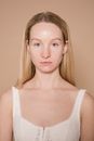 Emotionless female model with long hair showing natural skin looking at camera against beige background