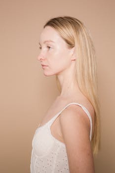 Side view portrait of a young woman with long hair against a beige background in a studio setting.