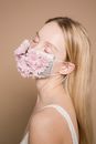 Side view of peaceful female with closed eyes wearing colorful flower mask standing on beige background during disease pandemic in studio