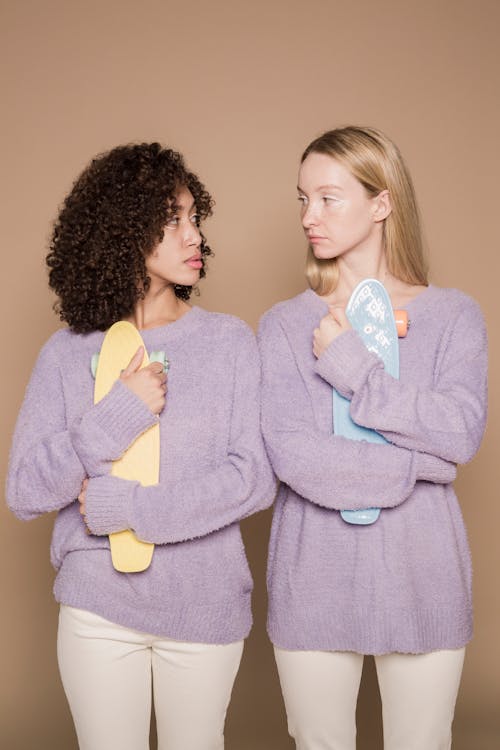 Multiethnic friends with modern skateboards looking at each other on beige background of studio