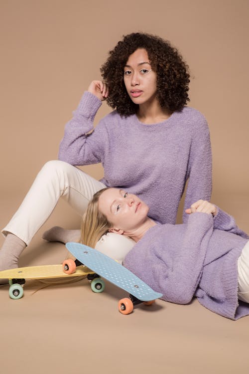 Diverse friends in casual pastel clothes relaxing and looking at camera on beige background of studio with skateboards