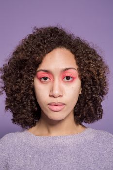 Young ethnic female with short dark curly hair looking at camera on purple background