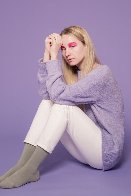 Full body of female with long hair and pink eyeshadows looking at camera on purple background of studio