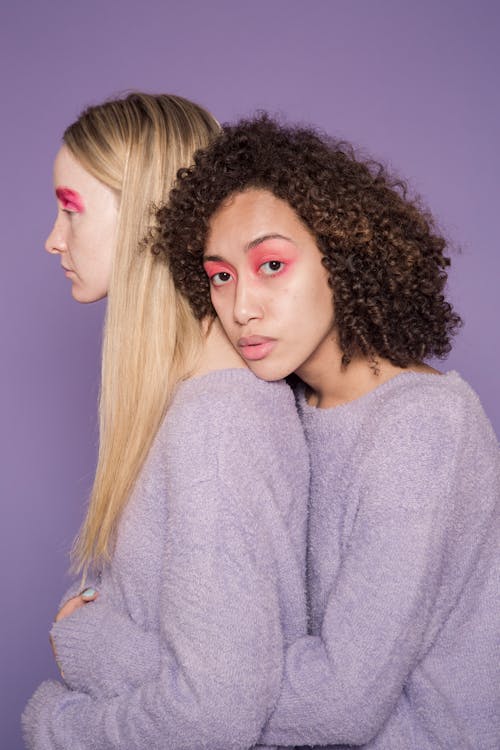 Multiracial women with bright pink eyeshadows embracing