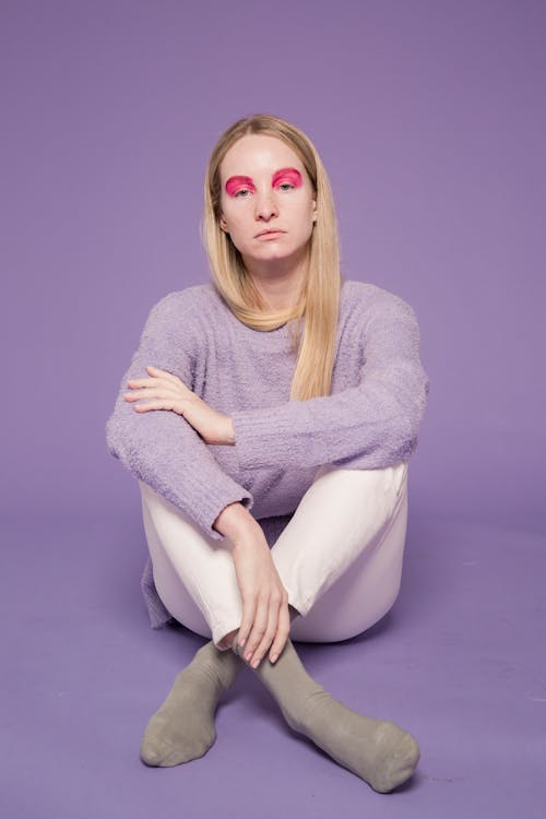 Young slender female with extraordinary makeup looking at camera on purple background of studio