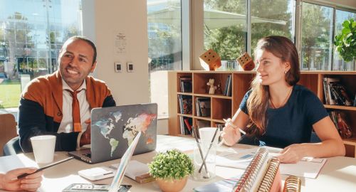 Free Colleagues engaging in a collaborative meeting with laptops and paperwork in a sunlit office. Stock Photo