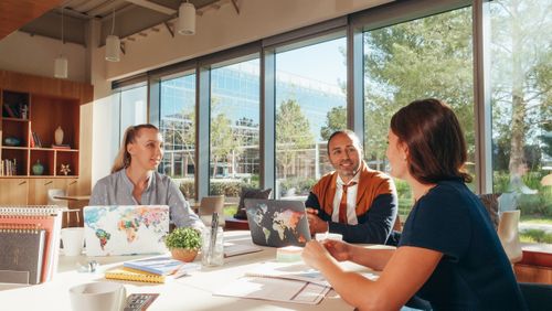 Free Three diverse professionals collaborate in a bright, modern workspace. Stock Photo