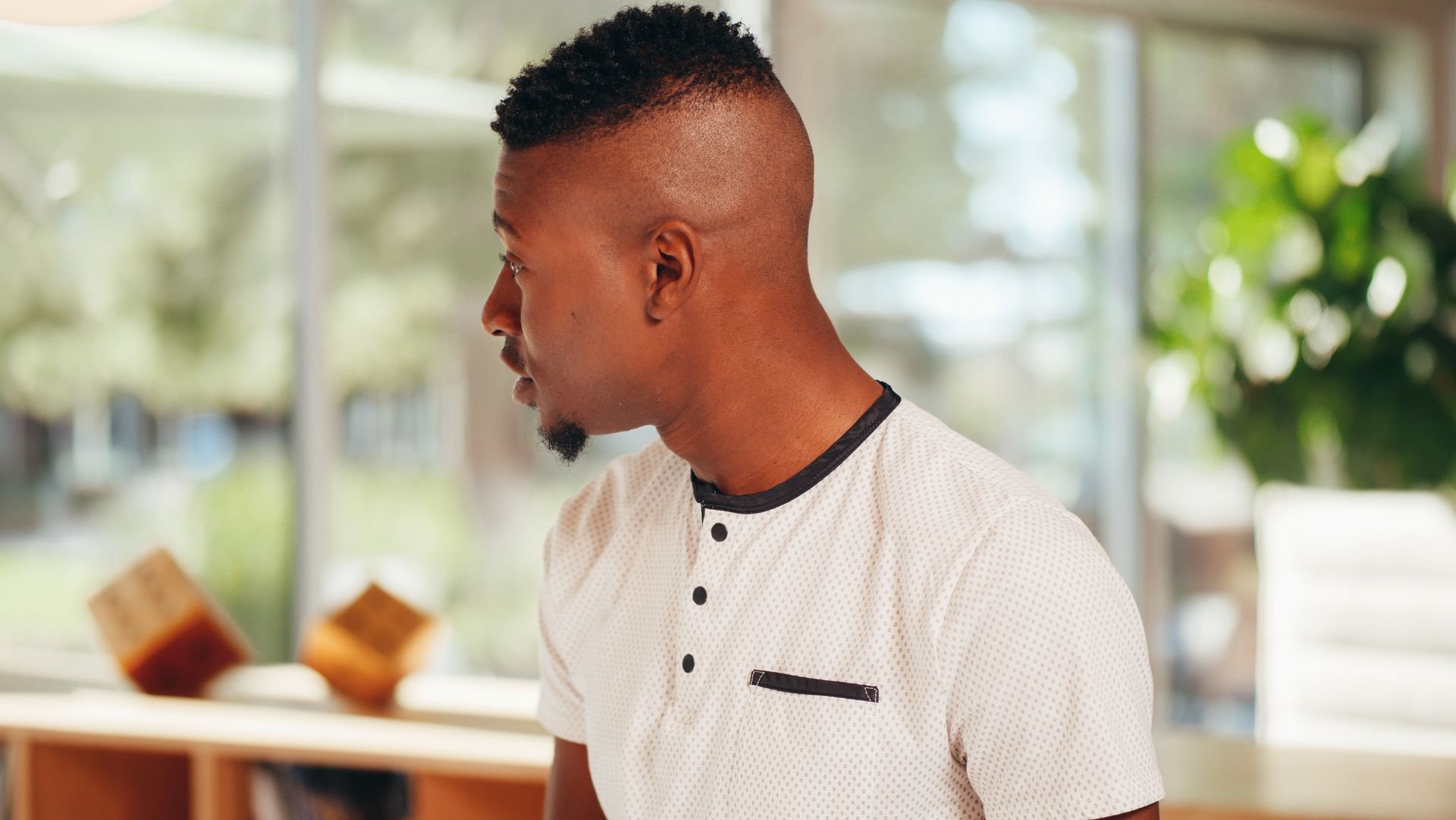 A young man in a modern office setting gazing thoughtfully out the window.