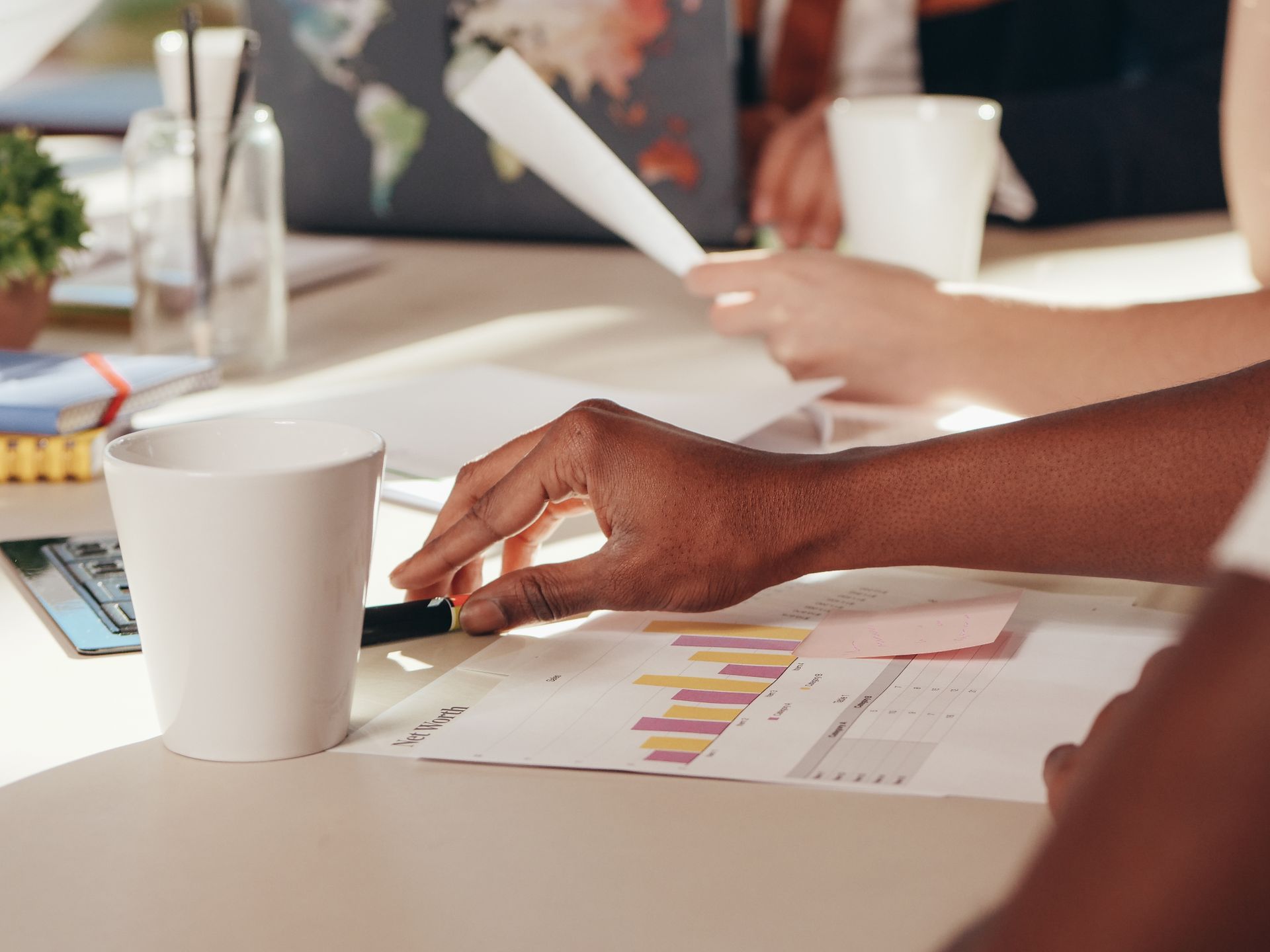 Close-up of business meeting with hands analyzing graphs, using technology and enjoying coffee.