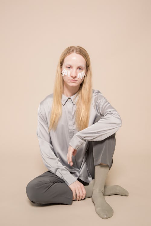 Calm young lady with chamomile petals on face looking at camera against beige background