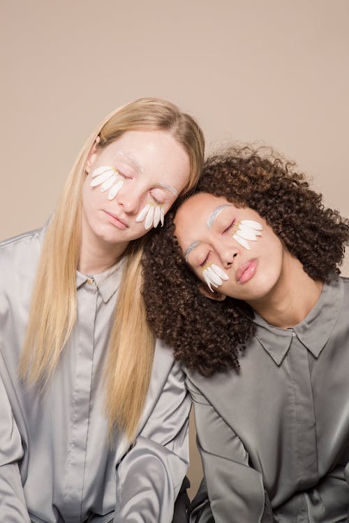 Calm young diverse ladies with closed eyes and flower petals on faces