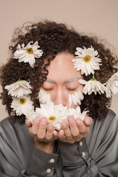 Young ethnic woman smelling fresh chamomile flowers with closed eyes