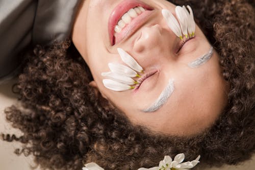 Delighted young ethnic woman smiling with closed eyes during skin care treatment