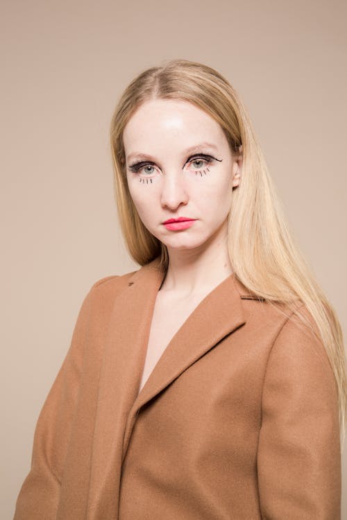Emotionless female with extraordinary makeup on face looking at camera on beige background of studio