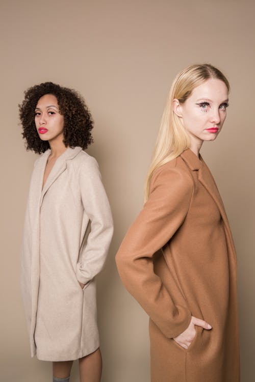 Confident multiethnic friends in stylish oversize coats looking at camera on beige background