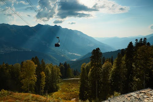 Picturesque landscape of cable car moving over scenic valley in mountains covered with green grass and high trees during sunny day under blue sky