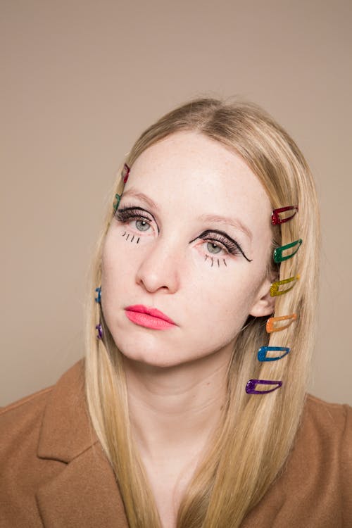 Young female with unusual expressive makeup on face and fair hair looking at camera on beige background