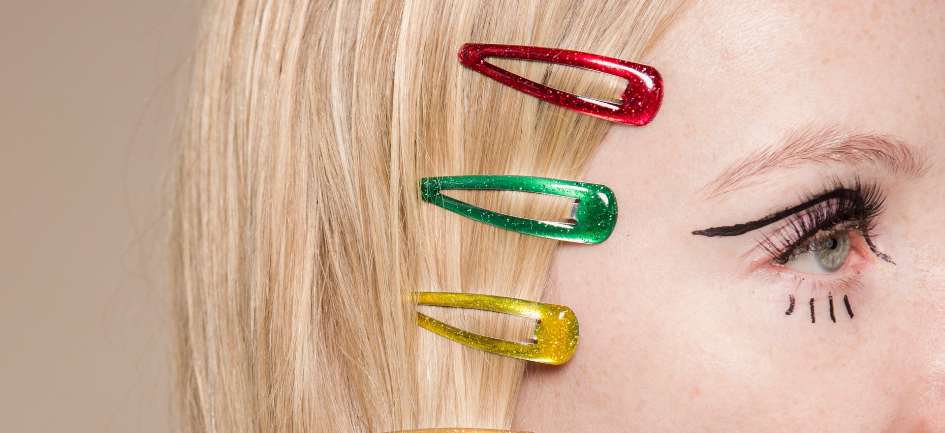 Crop anonymous female with red green and yellow hair clips on head on beige background