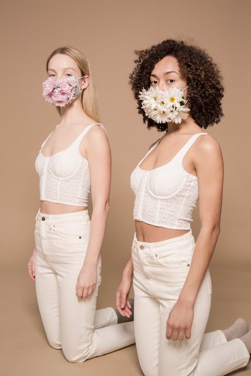 Diverse slender friends in white trousers looking at camera on beige background of studio