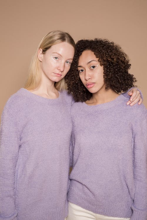 Diverse trendy friends in stylish purple warm sweaters looking at camera on beige background