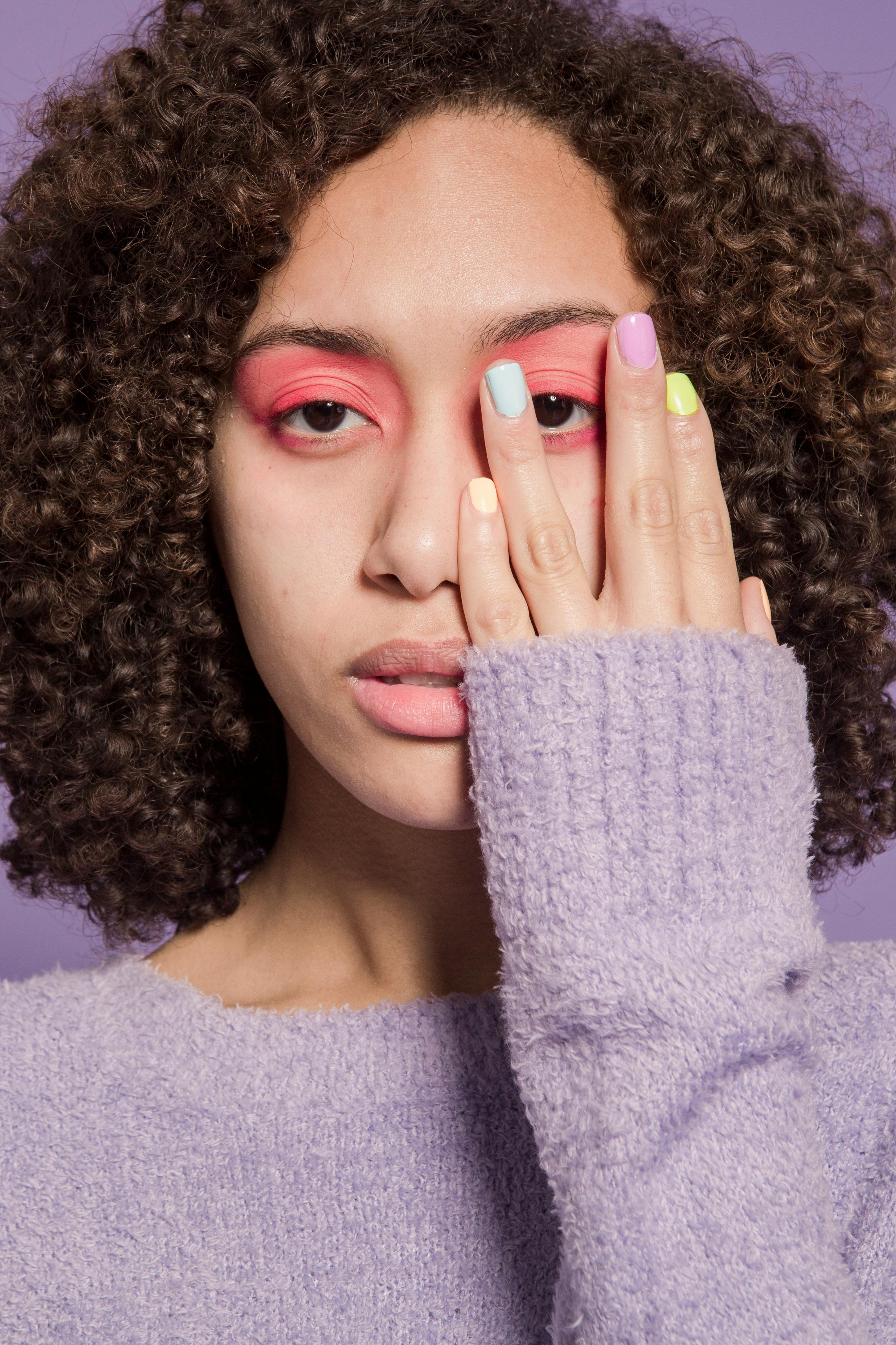 Crop ethnic female with pastel nails and curly dark hair looking at camera on purple background