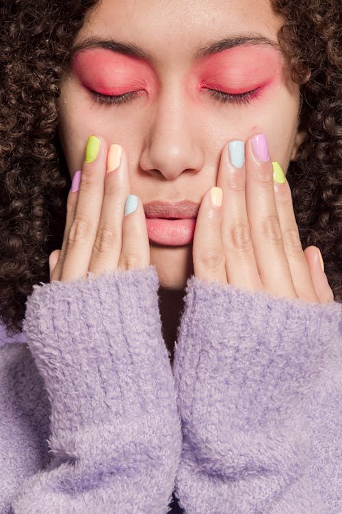 Thoughtful ethnic woman touching face with hands with pastel nail polish shades