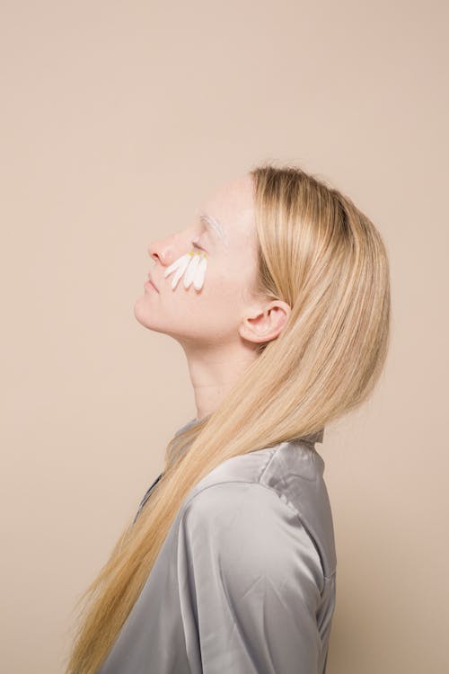 Side view of female with fair hair and eyes closed on beige background of studio