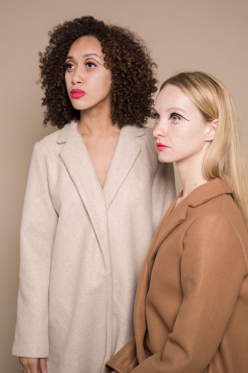 Free Serious young multiracial girlfriends in jackets with colorful makeup on face looking away in bright studio on beige background Stock Photo