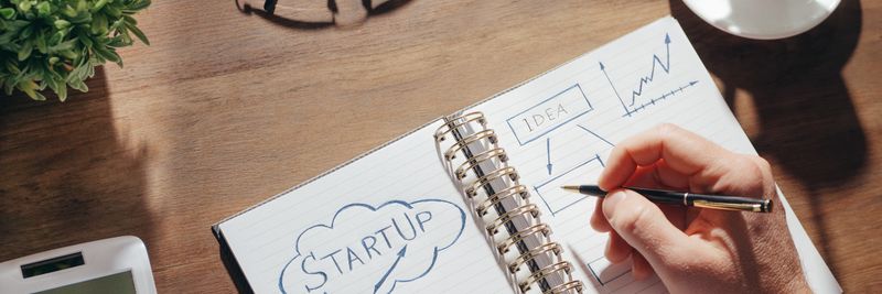 A creative workspace featuring startup planning on a notepad, eyeglasses, and a cup of coffee.