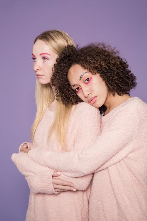 Multiracial women with bright makeup embracing in studio