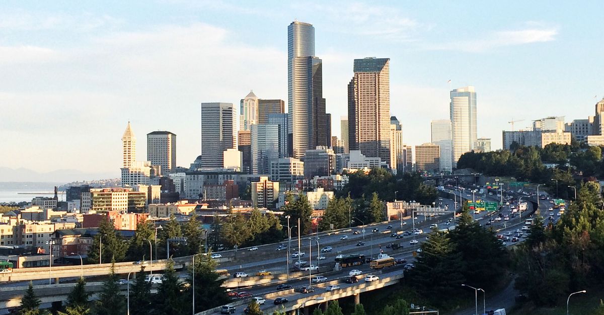 Panoramic view of Seattle's skyline and highway with bustling traffic under a clear sky.
