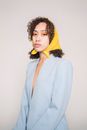 Fashionable young ethnic female model with dark curly hair in stylish blazer and kerchief on head standing in white studio and looking at camera