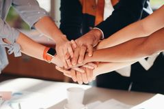 A close-up shot of diverse team members stacking hands over a white table, symbolizing unity and collaboration.