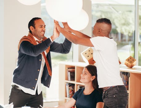 Three colleagues celebrating a success with a high-five gesture in a bright office space.