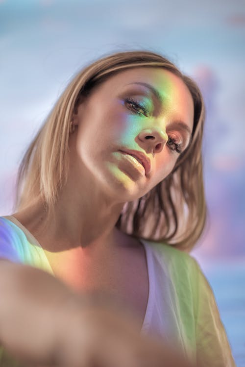 Portrait of charming young blonde female with colorful light on face and body looking at camera