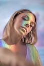 Portrait of charming young blonde female with colorful light on face and body looking at camera