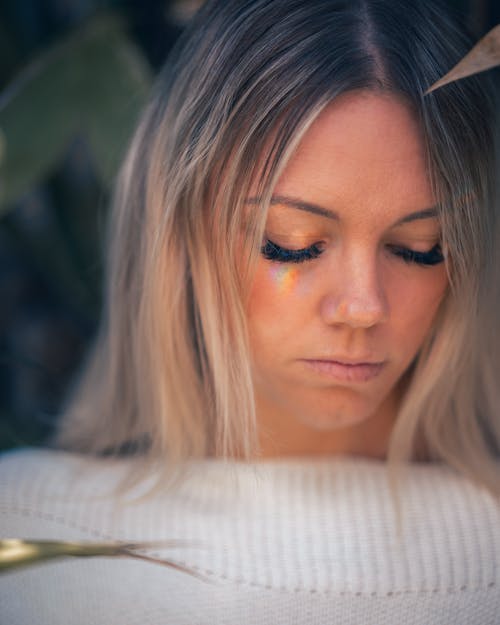 Free Upset pensive female with makeup and sorrow facial expression in white sweater standing near plants at home Stock Photo