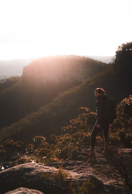 Side view of male hiker with backpack admiring picturesque scenery while walking on mountainside in back lit