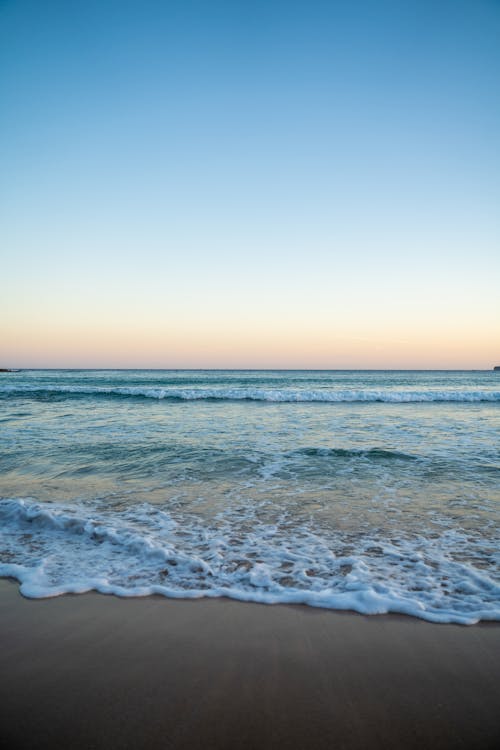 Spectacular view of wavy ocean with foamy water running on wet empty coastline under colorful sky at sunset