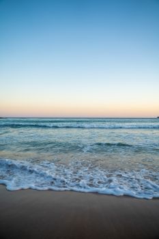 Spectacular view of wavy ocean with foamy water running on wet empty coastline under colorful sky at sunset