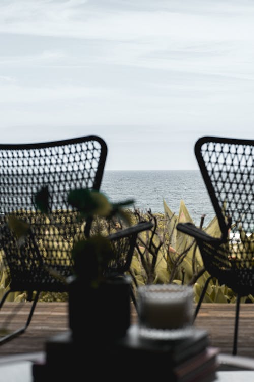 Free Wooden terrace with wicker armchairs placed nearby lush greenery in front of endless rippling seawater Stock Photo
