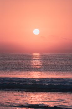 Spectacular scenery of bright colorful sundown reflecting in rippled sea water washing coastline with waves