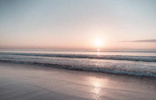 Scenic seascape with wavy tide washing wet coastline under clear gray sky with yellow stripe of dusk