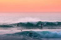 日落时分，冲浪者在明亮的橙色天空下征服汹涌大海的泡沫翻滚波浪的风景如画