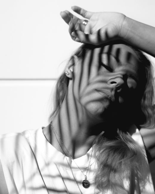 Black and white portrait of young female with shadow from frond on face fair hair with hand on head and closed eyes standing on white background with gray horizontal line