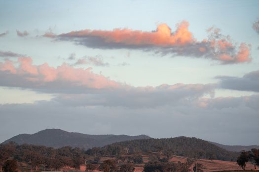 Serene hilly landscape with colorful clouds at sunset, perfect for nature scenes.
