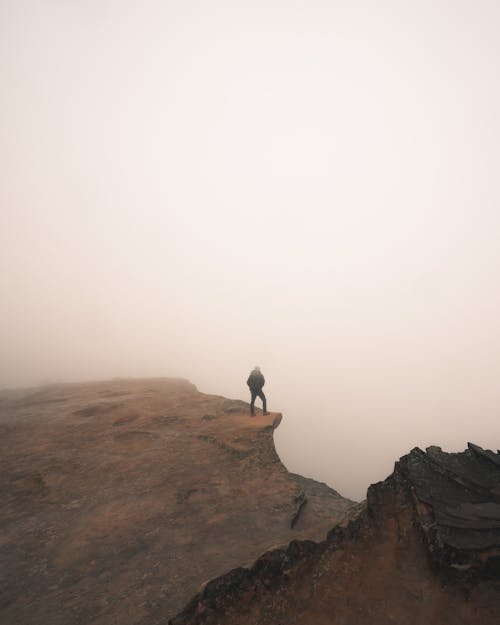 Person Standing on a Cliff during Foggy Weather