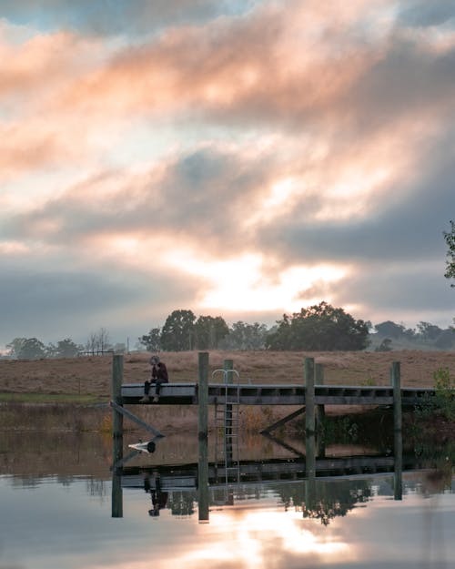 Person Sitting at the End of a Pier at Sunset 