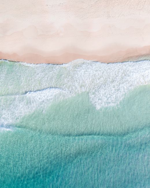 Stunning aerial view of Shoal Bay beach in NSW, Australia with crystal clear waves crashing on the sand.